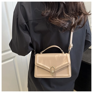Detail of beige crossbody bag featuring an oval gold swivel lock and a sleek flap design
