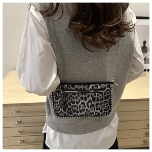 Detail van luipaardprint crossbodytas met zilveren ketting en metalen klinknagelrand