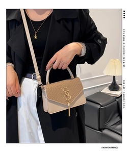 Detail of woven flap and gold S-buckle on a beige crossbody bag worn with a black coat