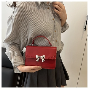 Detail of red leather crossbody bag featuring a metallic silver bow and chain strap