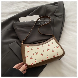 Detail of cream shoulder bag with cherry print and brown leather trim on grey blazer