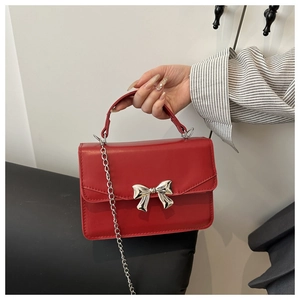 Detailed macro view of the red leather bag featuring a silver bow-knot metal ornament