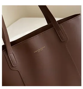 Close-up of deep brown leather tote bag with gold logo and reinforced handle stitching