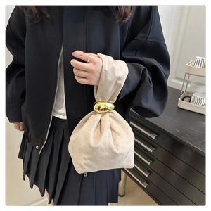 Close-up of the champagne fabric bucket bag featuring a polished gold metal buckle detail