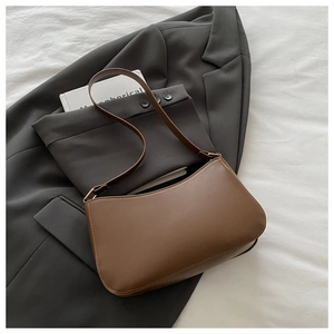 Close-up of a brown crescent shoulder bag styled on a grey blazer with a book