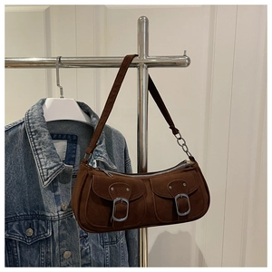 Détail du sac sous l'aisselle en daim marron café avec boucles argentées et chaîne sur denim