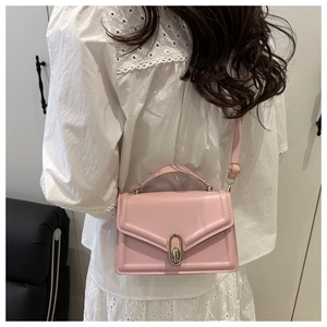 Detail of pink small square bag with golden oval swivel lock on leather exterior