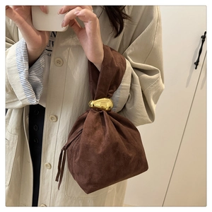 Close-up of brown suede drawstring bucket bag with a glossy gold teardrop metal buckle