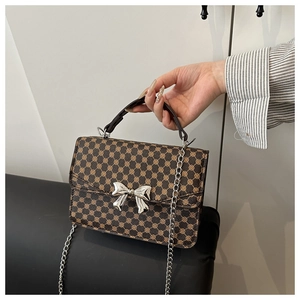 Detailed view of silver bow-shaped metal buckle and brown geometric pattern on a crossbody bag