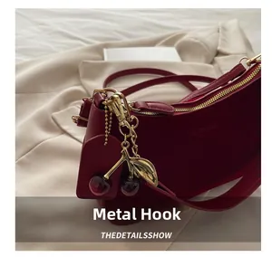 Détail du sac bandoulière en cuir rouge avec attaches dorées et pendentif cerise