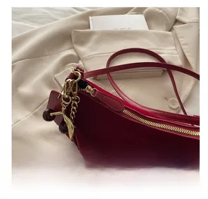 Détail d'un sac demi-lune bordeaux avec fermeture éclair dorée et breloque cerise