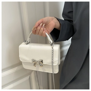 Detail of white leather mini bag with silver metal bow and chain strap