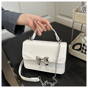 Close-up of white leather square bag with silver metal bow clasp and chain strap