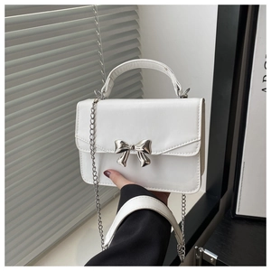 Detail shot of white leather bag with silver bow buckle and elegant metal chain strap