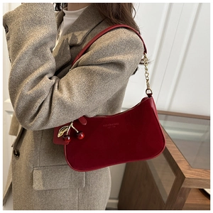 Détail du sac baguette en cuir rouge avec breloque cerise porté sur un blazer gris