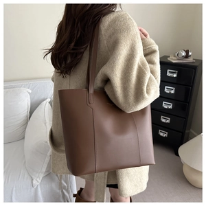 Detail of large brown leather tote bag with vertical stitching and slim shoulder straps