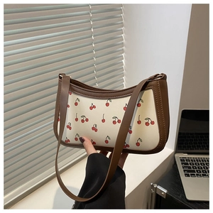 Close-up of cherry pattern handbag with brown leather trim and golden chain strap