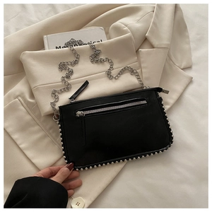 Detail van zwarte lederen handtas met zilveren studs, rits en zilveren kettingriem
