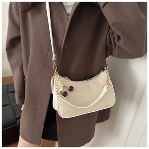 Détail d'un sac demi-lune beige avec breloque cerise et doubles bandoulières chic