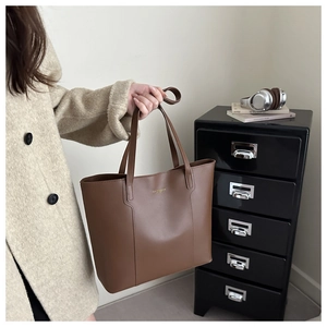 Detailed shot of large brown leather tote bag held by hand in a modern office setting