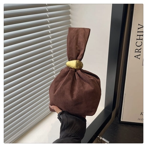 Detail of brown suede bucket bag featuring polished gold metal rings on the handle
