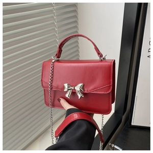 Close-up of red mini square bag featuring a silver metal bow and delicate chain strap