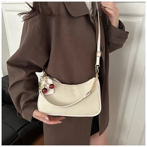 Détail d'un sac hobo beige avec breloque cerise rouge et bandoulière sur un manteau