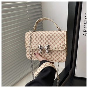 Detailed view of cream square bag featuring silver bow lock and metallic chain strap