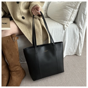 Detail of black leather tote bag with gold logo shown with casual commuting outfit