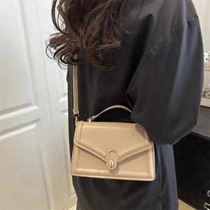 Minimalist beige leather handbag with gold oval clasp shown in a lifestyle crossbody view