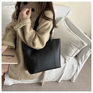 Detail of matte black leather tote bag showing soft texture and slim shoulder straps
