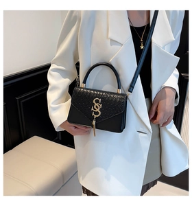 Detail of black faux crocodile leather handbag featuring gold S-logo and fringe tassel