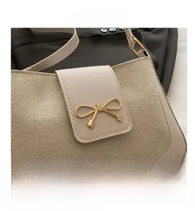 Detail of light beige shoulder bag featuring a golden bow-shaped clasp and mixed leathers
