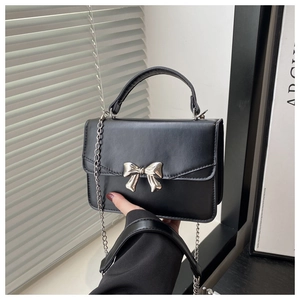 Detail of black mini crossbody bag featuring a silver metal bow clasp and chain strap