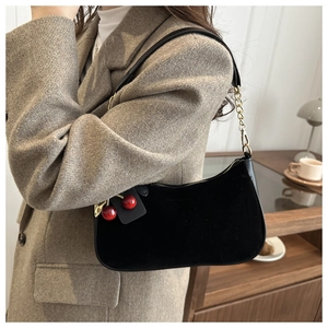 Détail du sac à bandoulière en velours noir avec pendentif cerise et chaîne dorée
