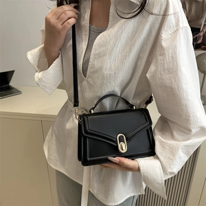 Minimalist black leather crossbody handbag with golden clasp shown on a model