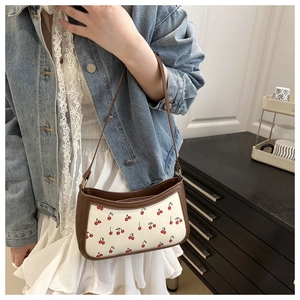 Detailed view of cherry print shoulder bag with brown trim on a lifestyle model