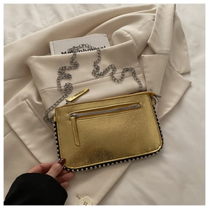 Detailopname van gouden crossbodytas met zilveren klinknagels en ketting schouderband