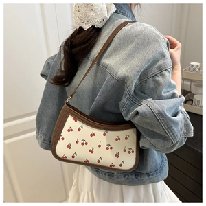 Detail of trendy cherry print shoulder bag with brown leather trim worn with denim jacket