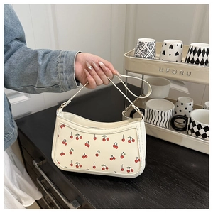 Detailed close-up of cream underarm bag featuring red cherry patterns and top handle