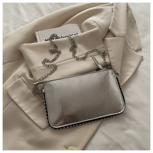 Detail van zilveren metallic crossbody tas met studs en ketting op neutrale blazer