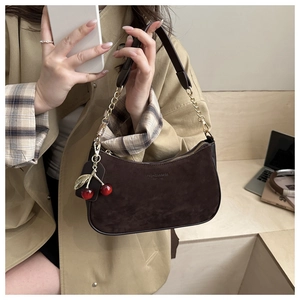 Détail du sac à bandoulière en daim marron foncé avec chaîne et pendentif cerise