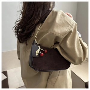 Détails d'un sac bandoulière en daim avec breloque cerise et chaîne dorée