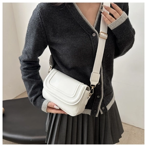Close-up of white saddle bag with fine stitching, gold hardware and wide fabric strap