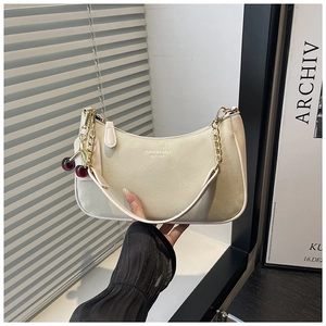 Détail d'un sac à main beige chic avec chaîne dorée élégante et un pendentif cerise