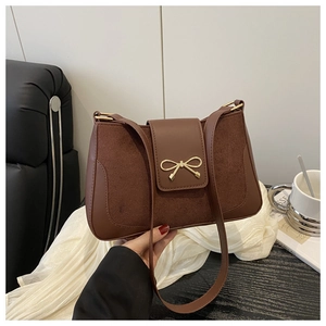 Detailed view of dark brown suede shoulder bag with a gold metal bow ornament