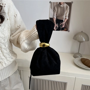 Elegant black velvet bucket bag with a large gold metal handle in a minimalist interior