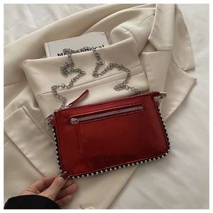 Detailopname van een rode metallic minitas met zilveren studs en een kettingriem