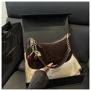 Détail d'un sac hobo en daim marron foncé avec chaîne dorée et breloque cerise