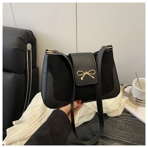Detail of black crossbody bag with gold bow buckle and mixed leather texture